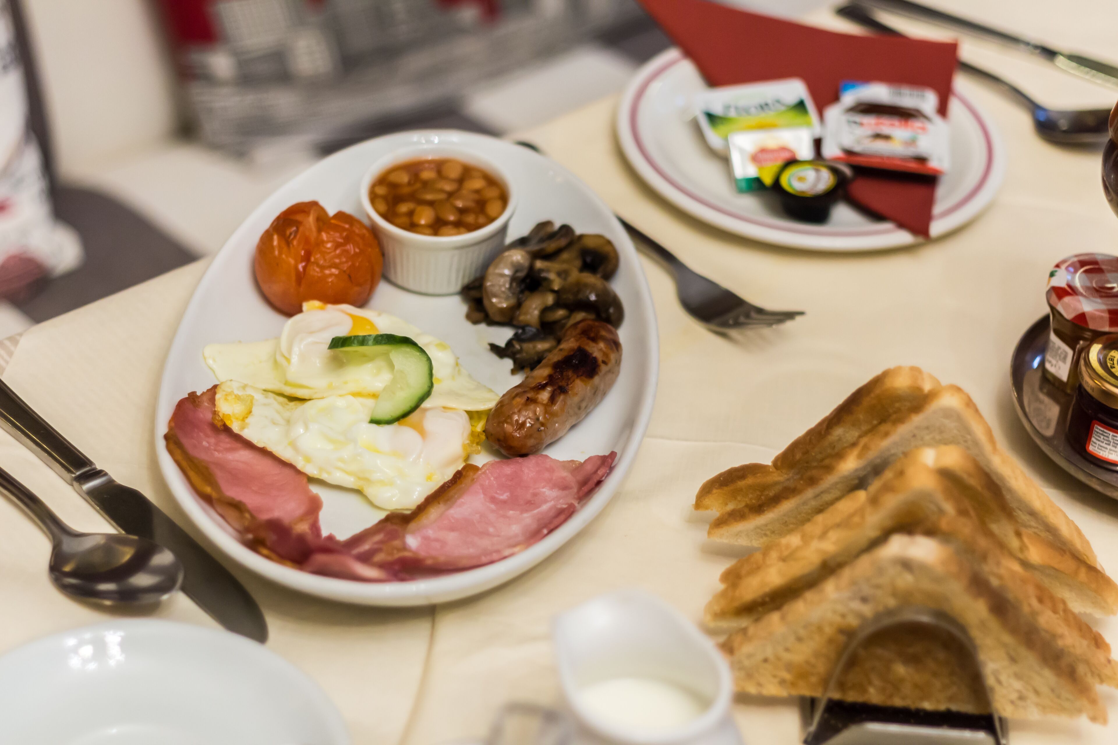 Ein Frühstücksteller mit Eiern, Speck, Würstchen, Pilzen, Bohnen und einer Tomate.