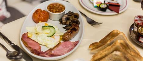 Ein Frühstücksteller mit Eiern, Speck, Würstchen, Pilzen, Bohnen und einer Tomate.
