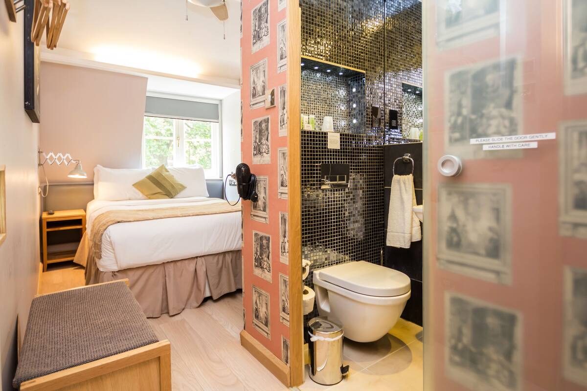 A compact hotel room with a bed, bedside table, and a small seating area.