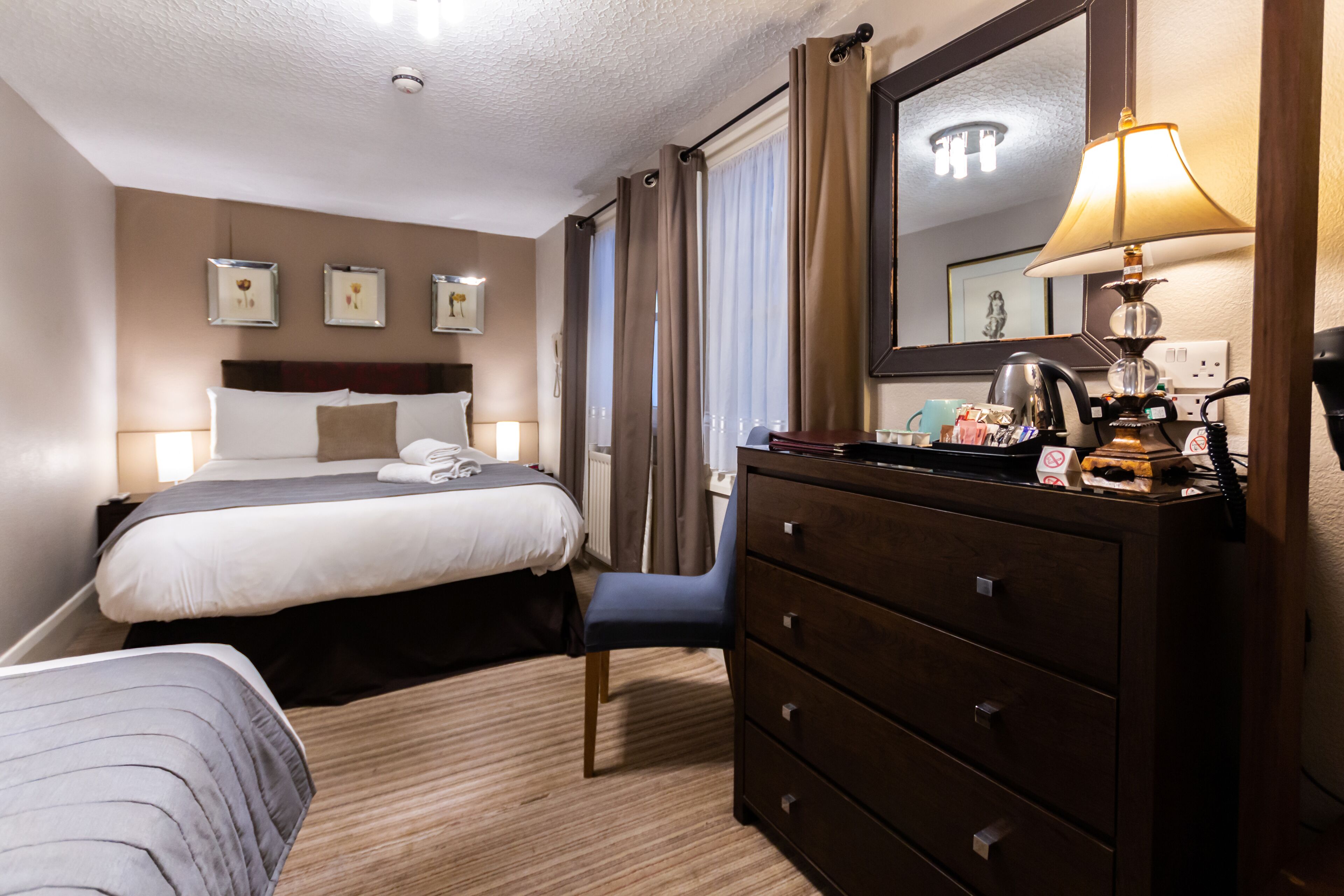 A hotel room with a bed, a dresser, a chair, and a mirror.