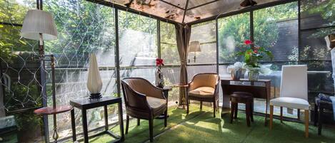A conservatory with a glass ceiling, green artificial grass, and furniture including chairs and a table.