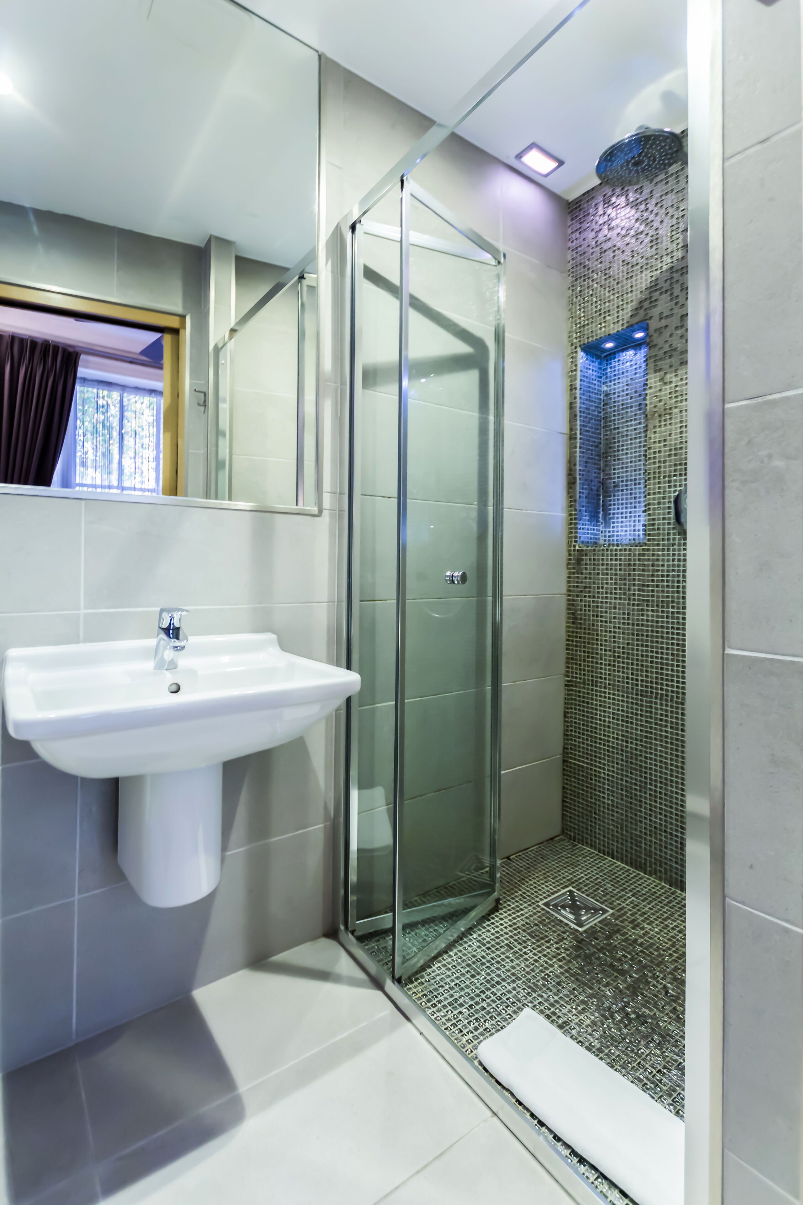 A modern bathroom with a glass-enclosed shower, a white sink, and tiled walls.