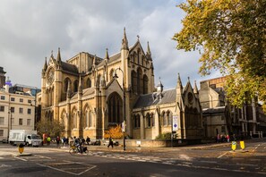 A historic church with Gothic architecture, a street in front, and a tree with autumn leaves. - Arosfa Hotel London by Compass Hospitality (London)