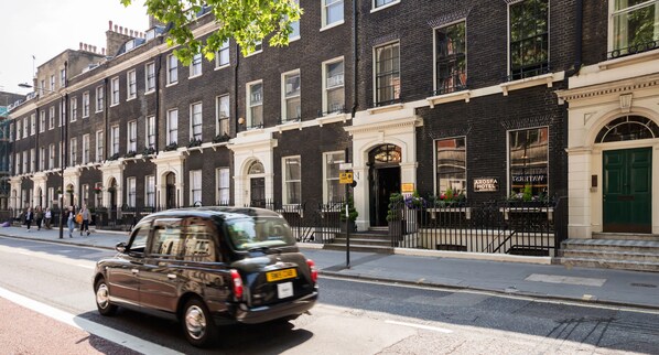A black taxi driving on a city street. - Arosfa Hotel London by Compass Hospitality (London)