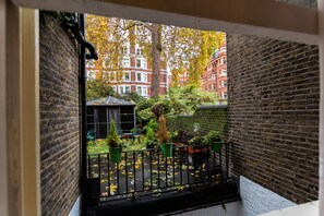 A courtyard with brick walls, a bench, potted plants, and a view of buildings in the background. - Arosfa Hotel London by Compass Hospitality (London)