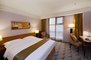Una habitación de hotel con una cama grande, dos sillones, un escritorio y una ventana con cortinas.