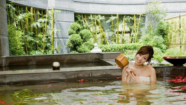 A person in a pool with water lilies and a bamboo backdrop.