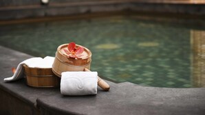A wooden container with a red flower on top, a white towel, and a stone bench by a pool.