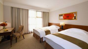 A hotel room with two beds, a desk with a chair, a lamp, and a large window with curtains.