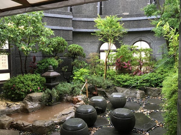 Un jardín japonés tradicional con un estanque de carpas koi, linternas de piedra y diversas plantas.