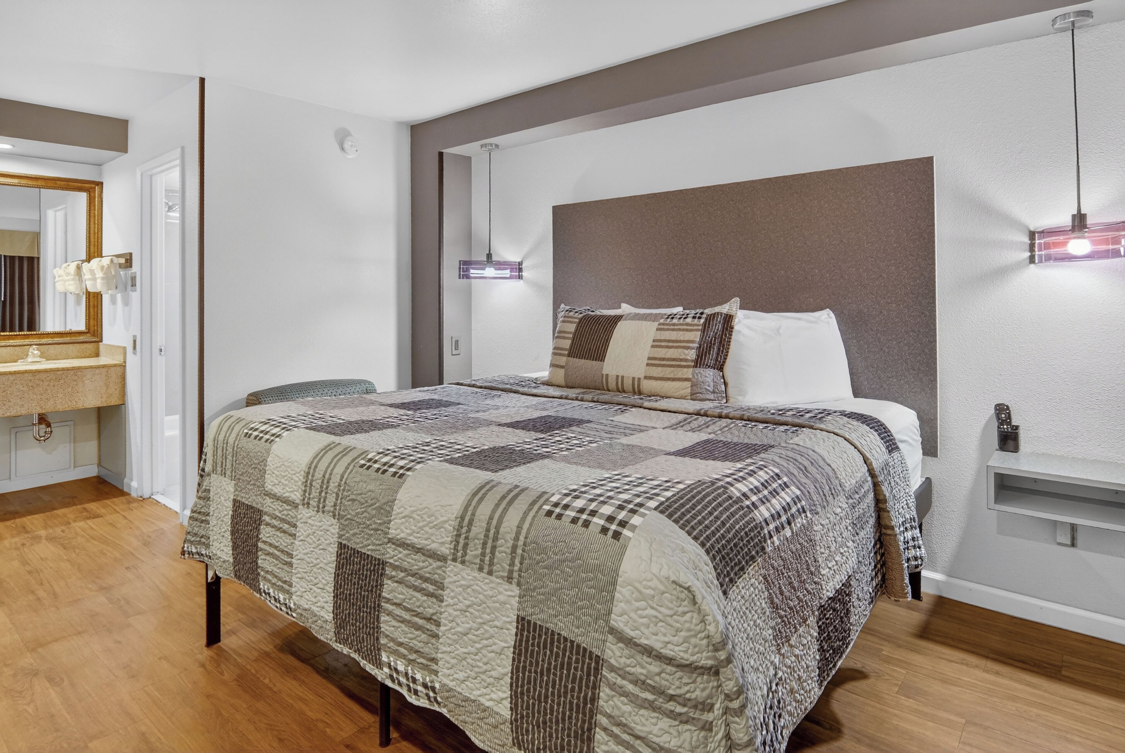 A bedroom with a large bed, a bedside table, a nightstand, a mirror, and a hanging light fixture.