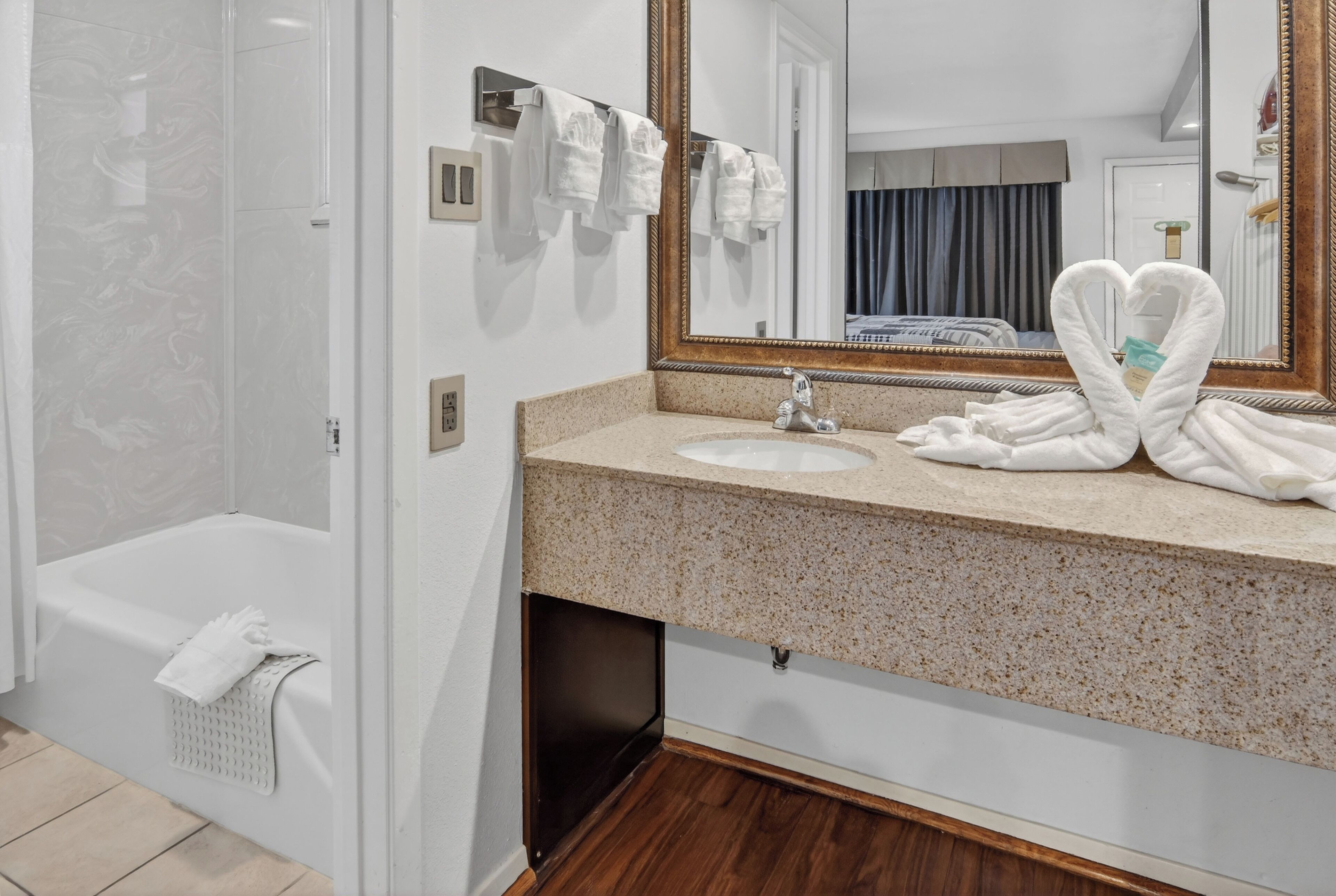 Une salle de bain avec une baignoire, un lavabo et un grand miroir. Des serviettes sont suspendues sur un porte-serviettes et une serviette est pliée en forme de cœur sur le lavabo.