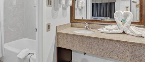 Une salle de bain avec une baignoire, un lavabo et un grand miroir. Des serviettes sont suspendues sur un porte-serviettes et une serviette est pliée en forme de cœur sur le lavabo.