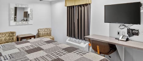 A hotel room with a large bed, a desk with a chair, a flat-screen TV, a mirror, and a window with curtains.