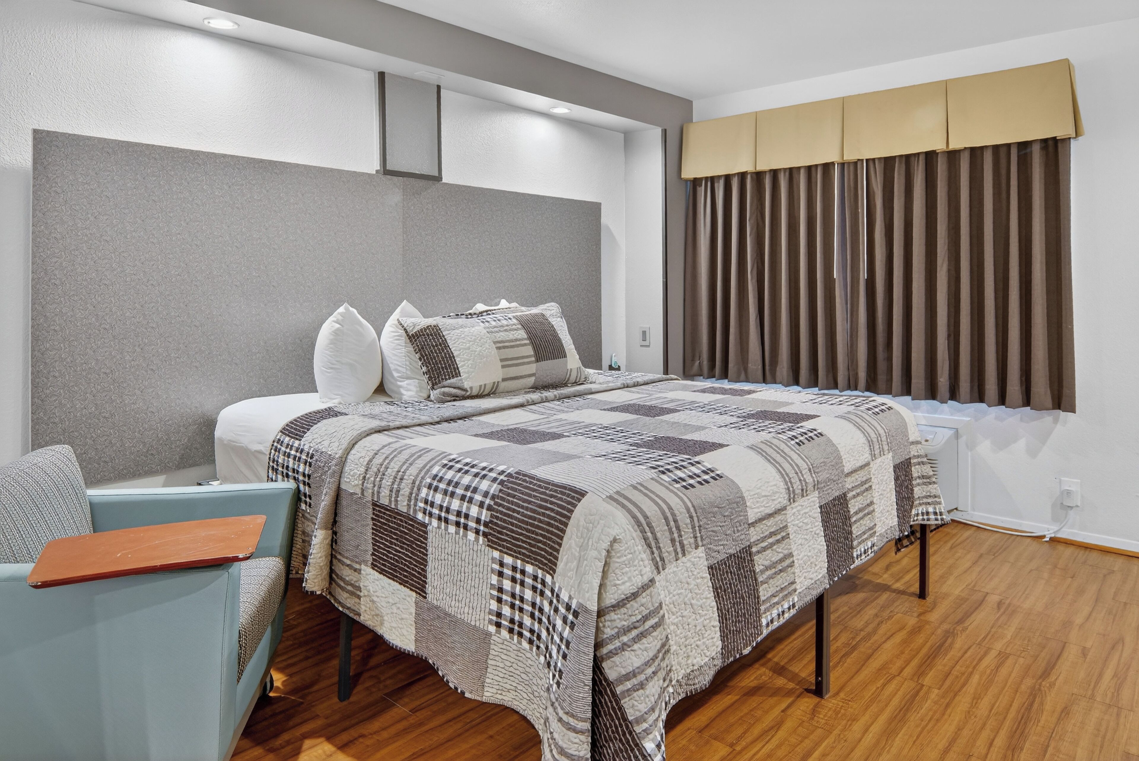 A modern bedroom with a large bed, a light blue armchair, and a window with curtains.
