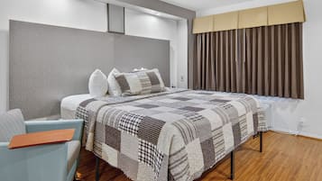 A modern bedroom with a large bed, a light blue armchair, and a window with curtains.