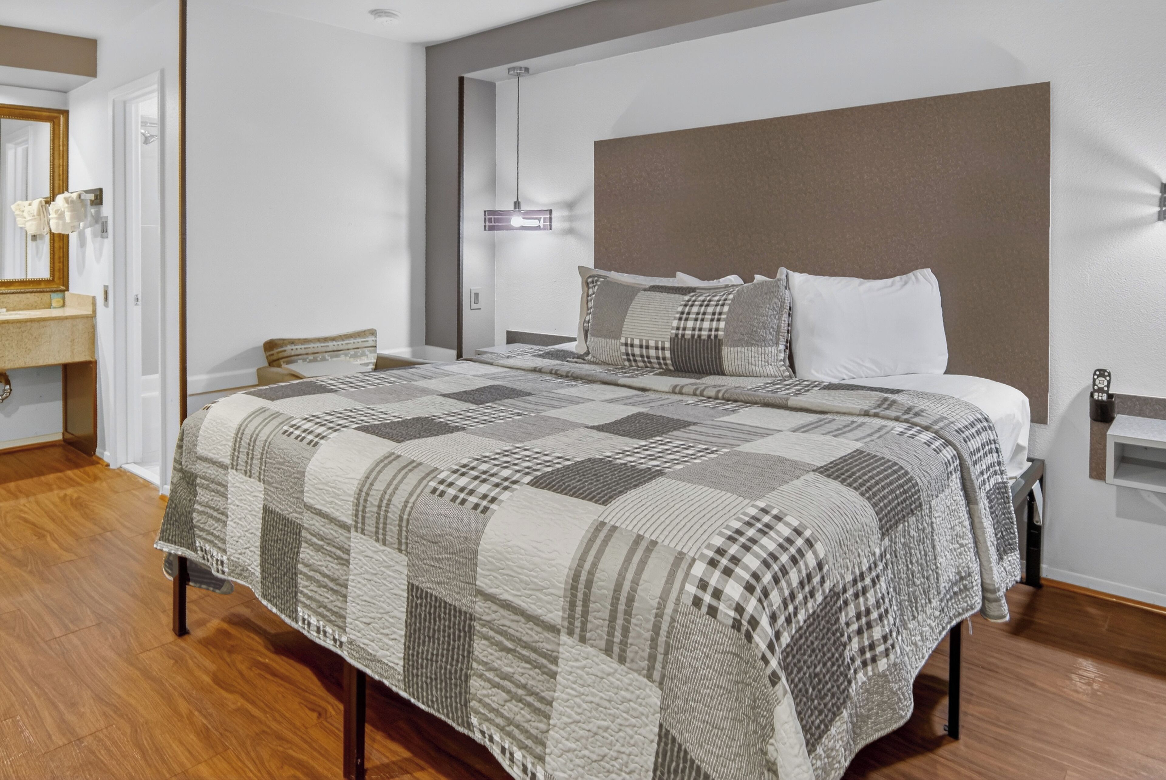 Un dormitorio moderno con una cama grande, una mesita de noche, una lámpara de pared y suelo de madera.