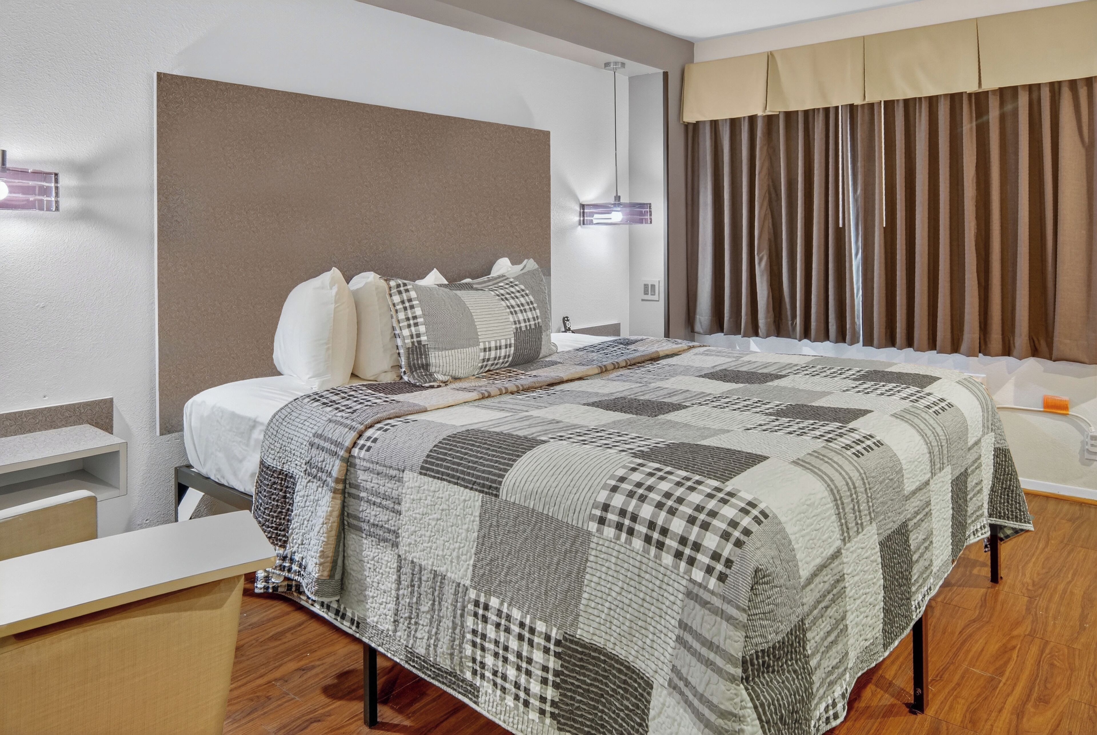 A hotel room with a large bed, a bedside table, a nightstand, a lamp, and a window with curtains.