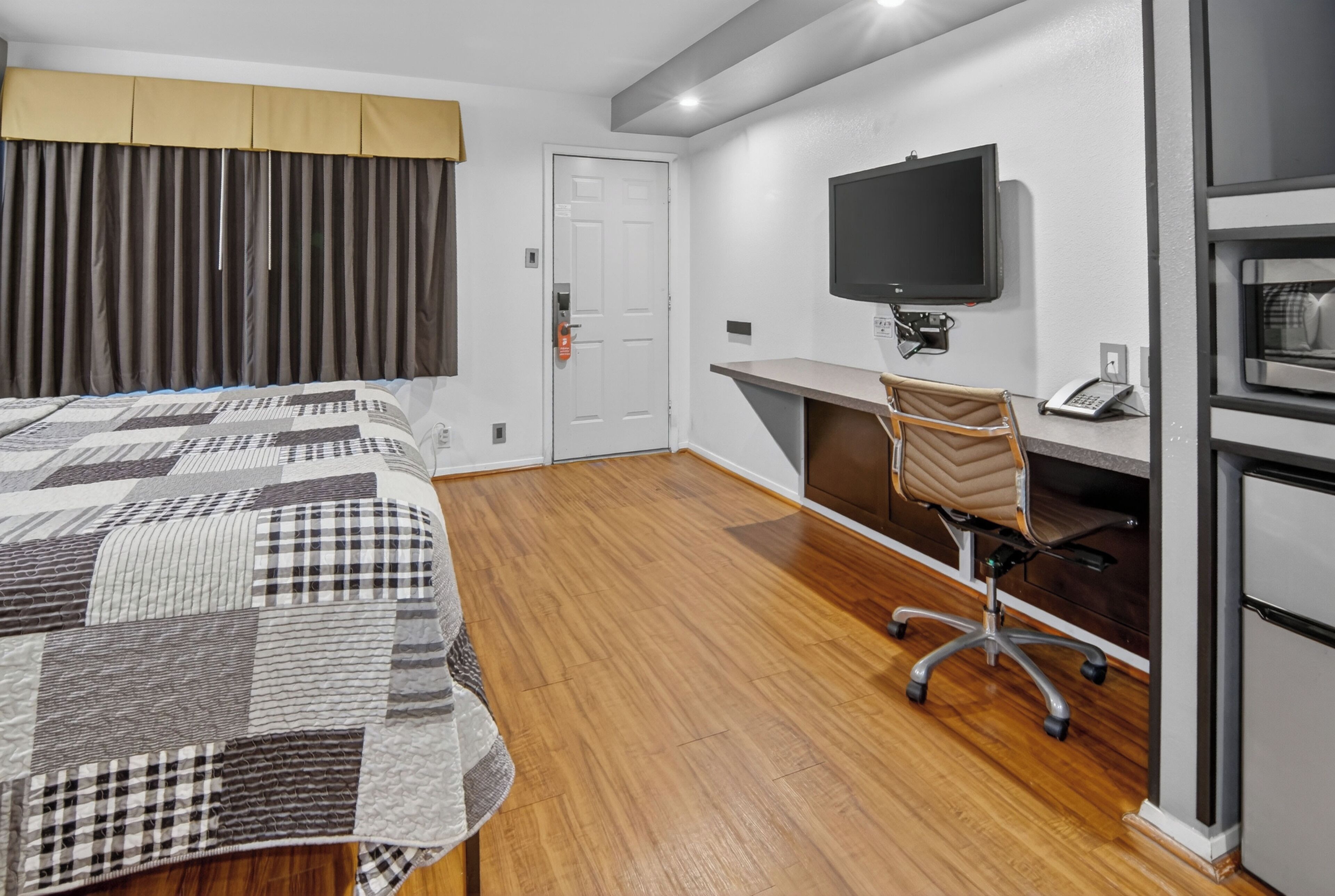 Una habitación de hotel con cama, escritorio con silla, televisor y refrigerador.