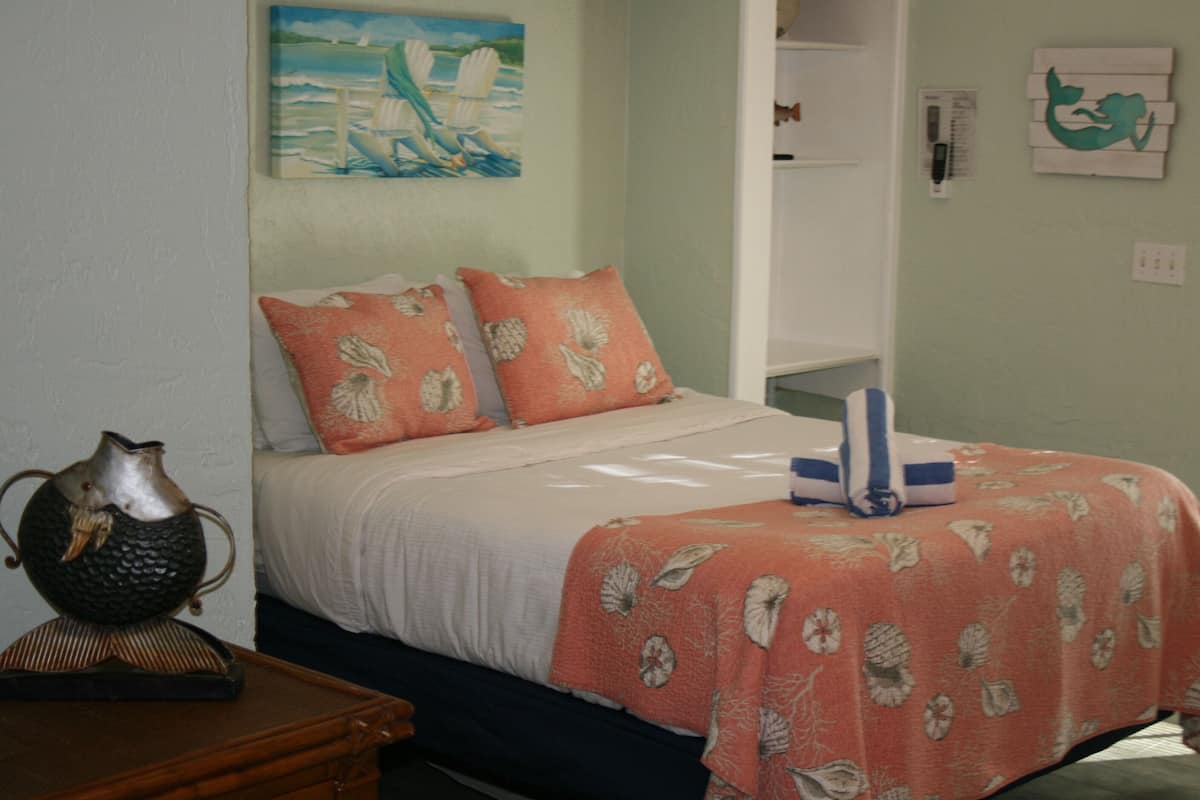 A neatly made bed with a floral bedspread, a decorative vase, and a painting of a sailboat on the wall.