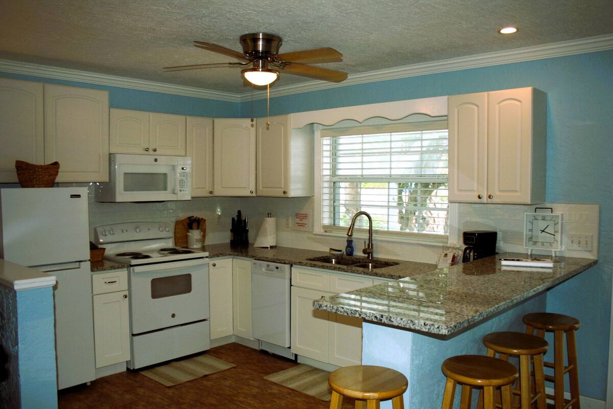 A kitchen with white cabinets, a microwave, stove, and a sink. There are three wooden stools at the island.