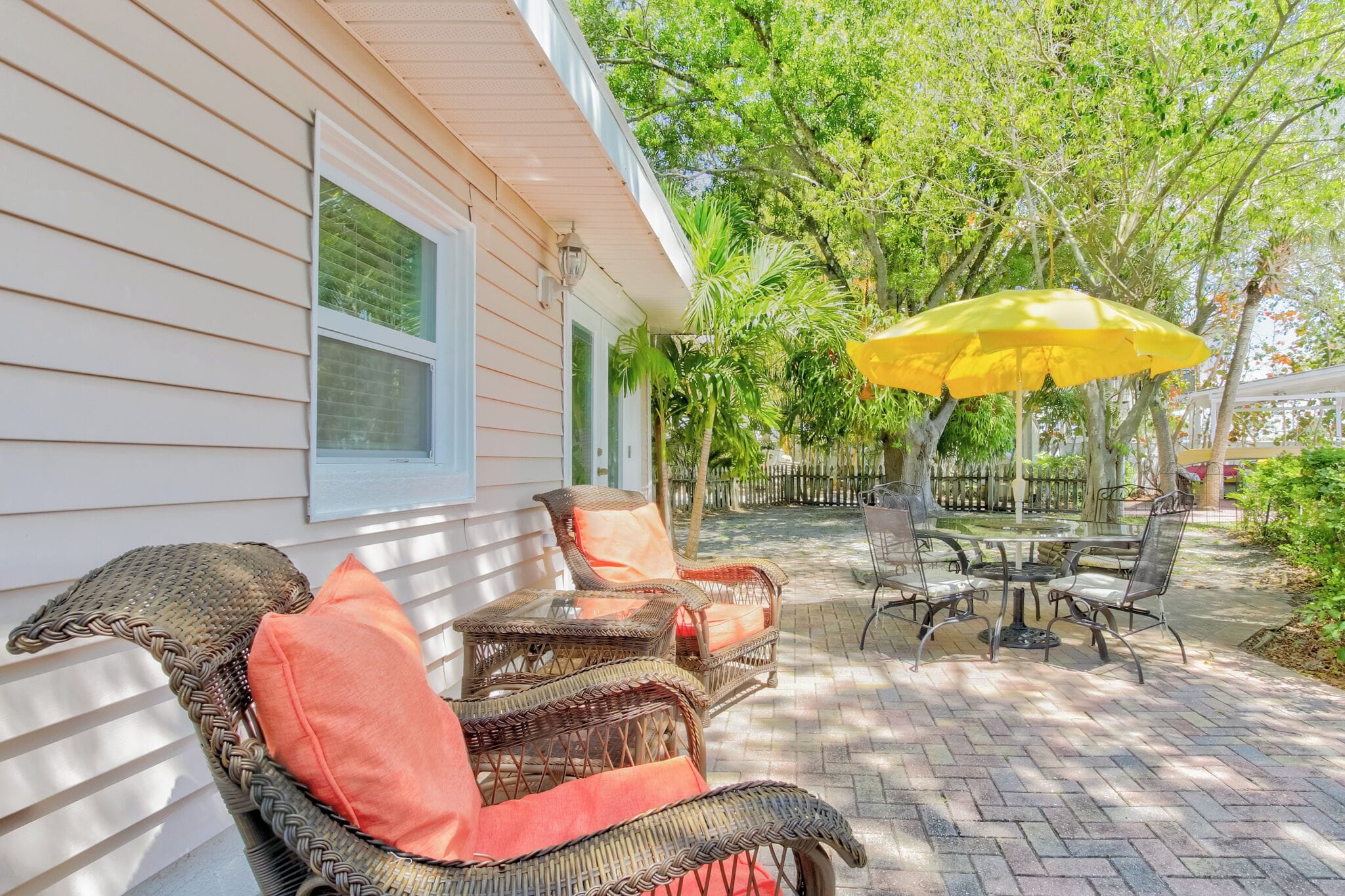 Une terrasse dotée de meubles en osier, d’un parasol jaune et d’un sol en briques.