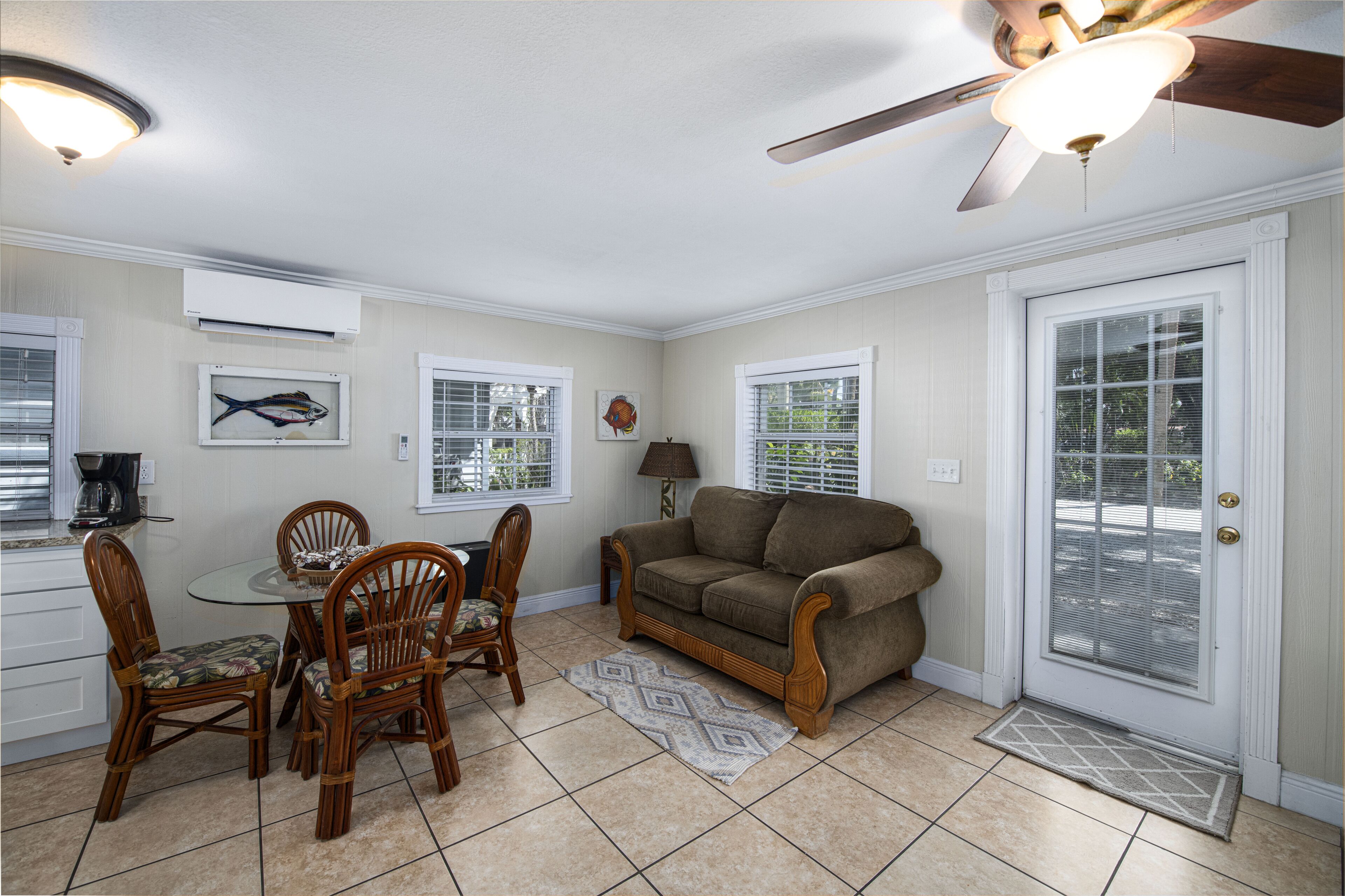 A dining area with a round table, four chairs, a brown sofa, and a ceiling fan.