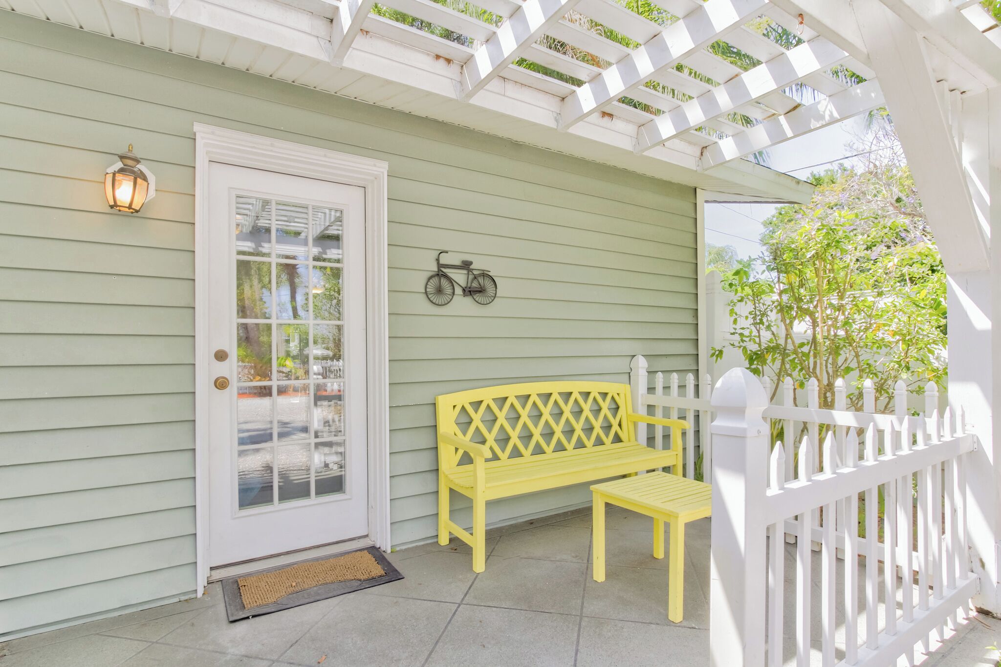A porch with a white picket fence, a yellow bench, and a bicycle mounted on the wall.