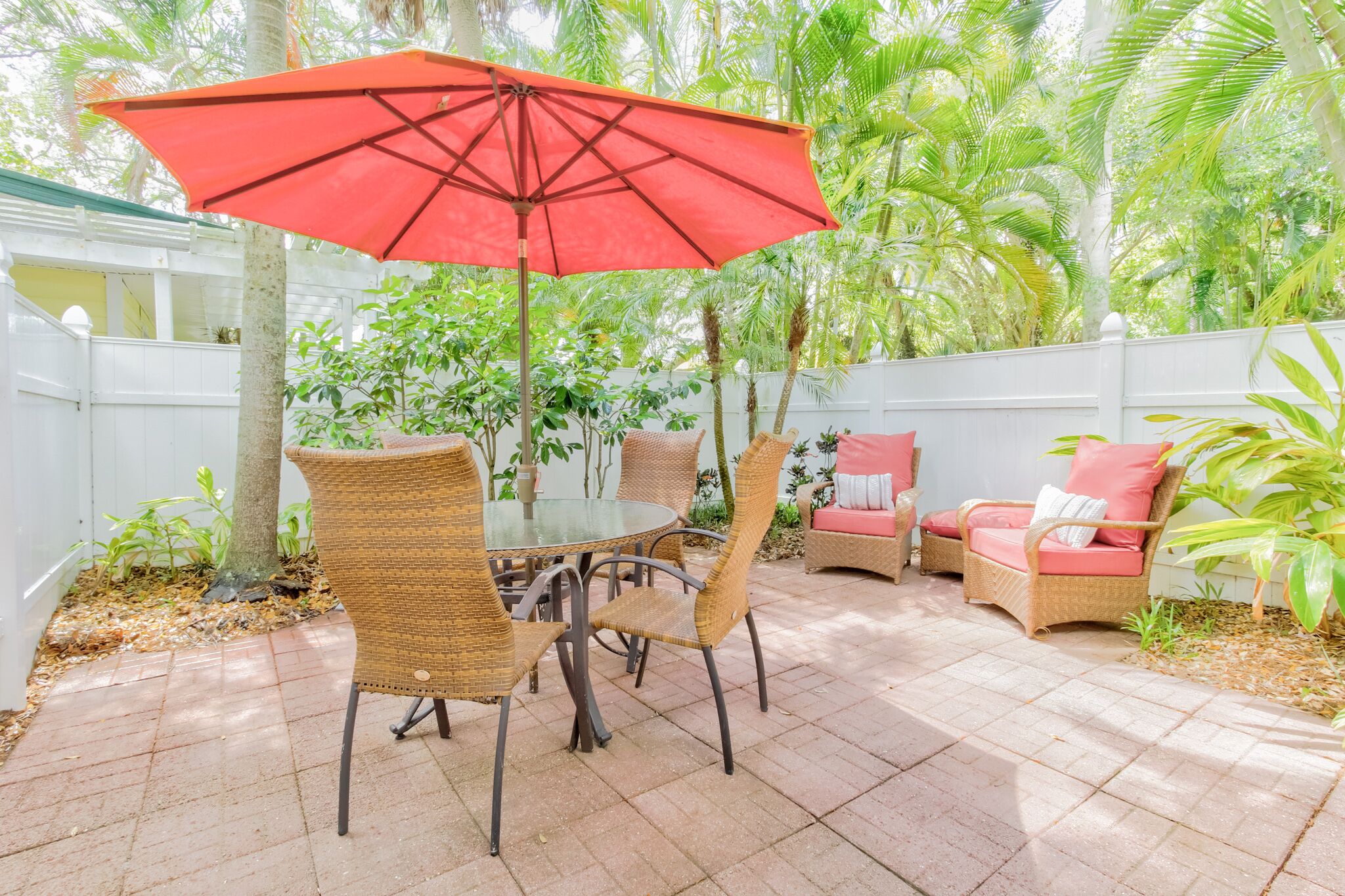 Une terrasse dotée de meubles en osier, d’un parasol rouge et d’une végétation luxuriante.