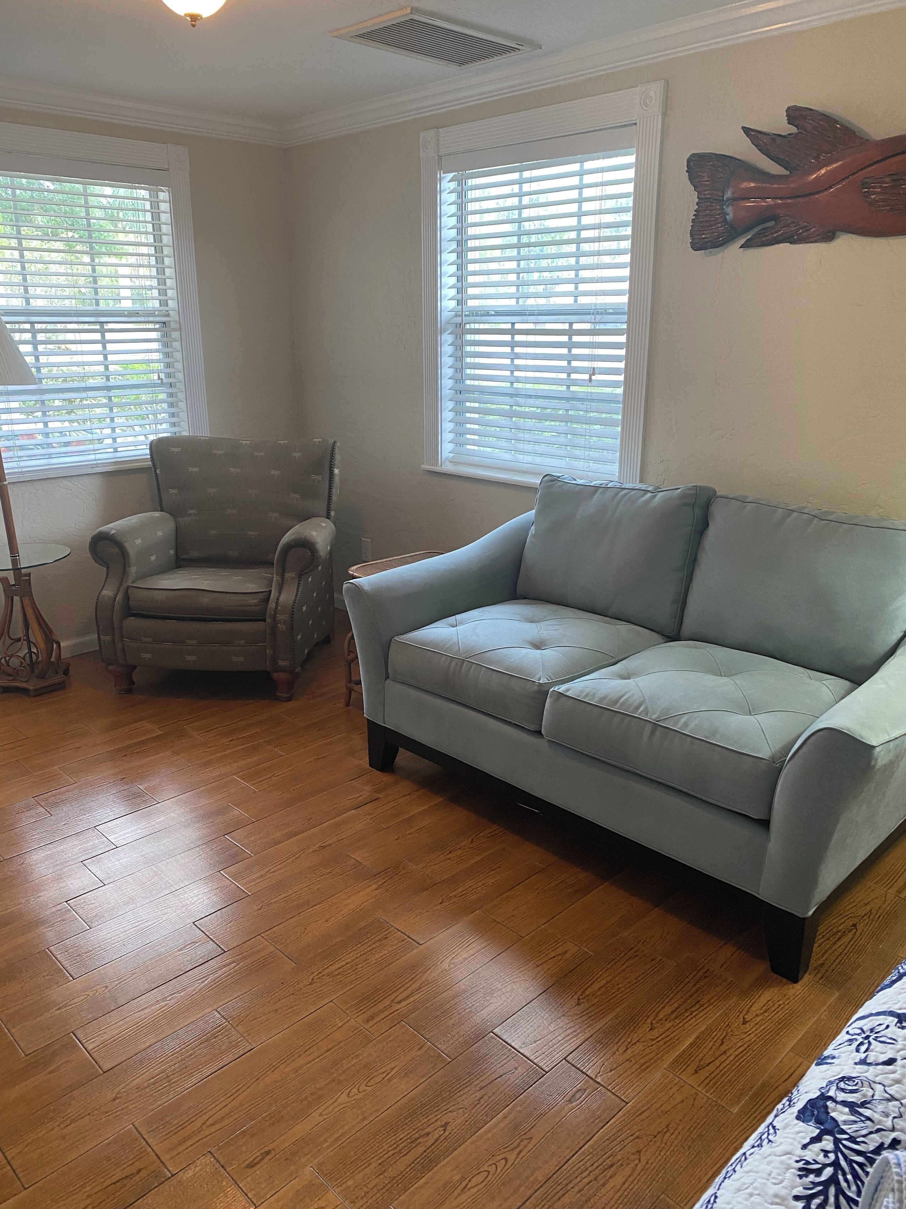 A living room with a light blue sofa, a patterned armchair, and a wooden floor.