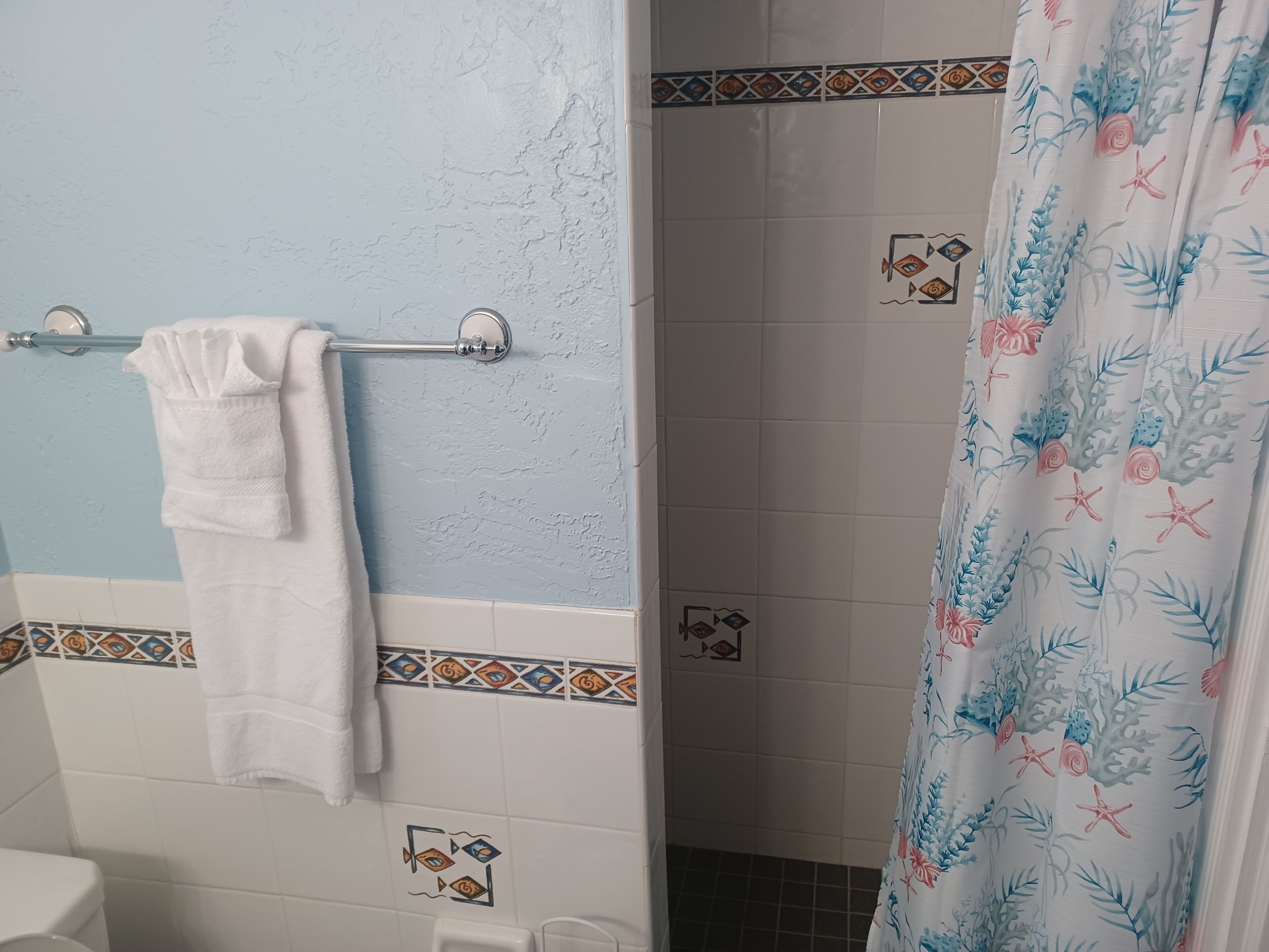 A bathroom with a towel rack, a shower curtain with a floral pattern, and decorative tiles.