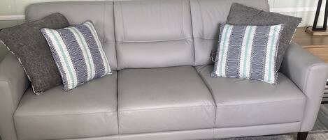 A grey leather sofa with patterned cushions against a herringbone-patterned rug. A vintage sign above reads "RYAN AND BURNS MARINE CHANDLERY SAN FRANCISCO".