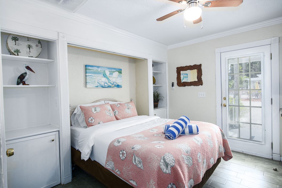 A bedroom with a bed, a ceiling fan, a door, and a window.