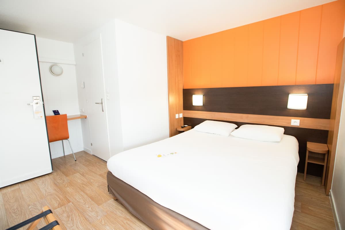 A hotel room with a large bed, a wooden headboard, a nightstand, a chair, and a wardrobe.