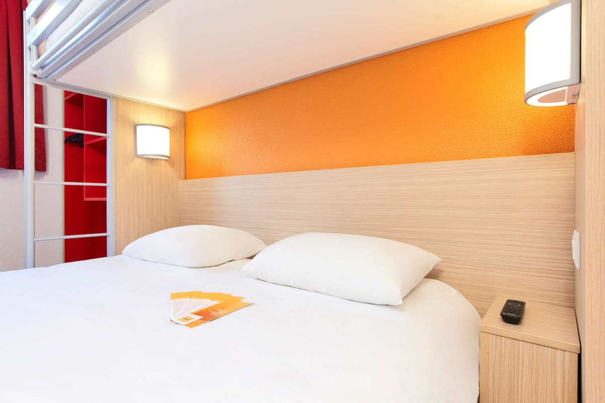 A hotel room with a bed, a nightstand, a red wardrobe, and a wall-mounted light fixture.