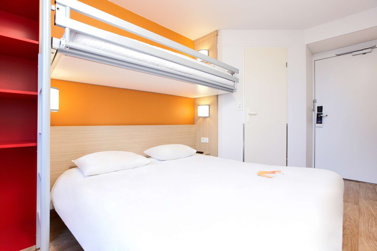 A hotel room with a bed, a red wardrobe, and a white door.