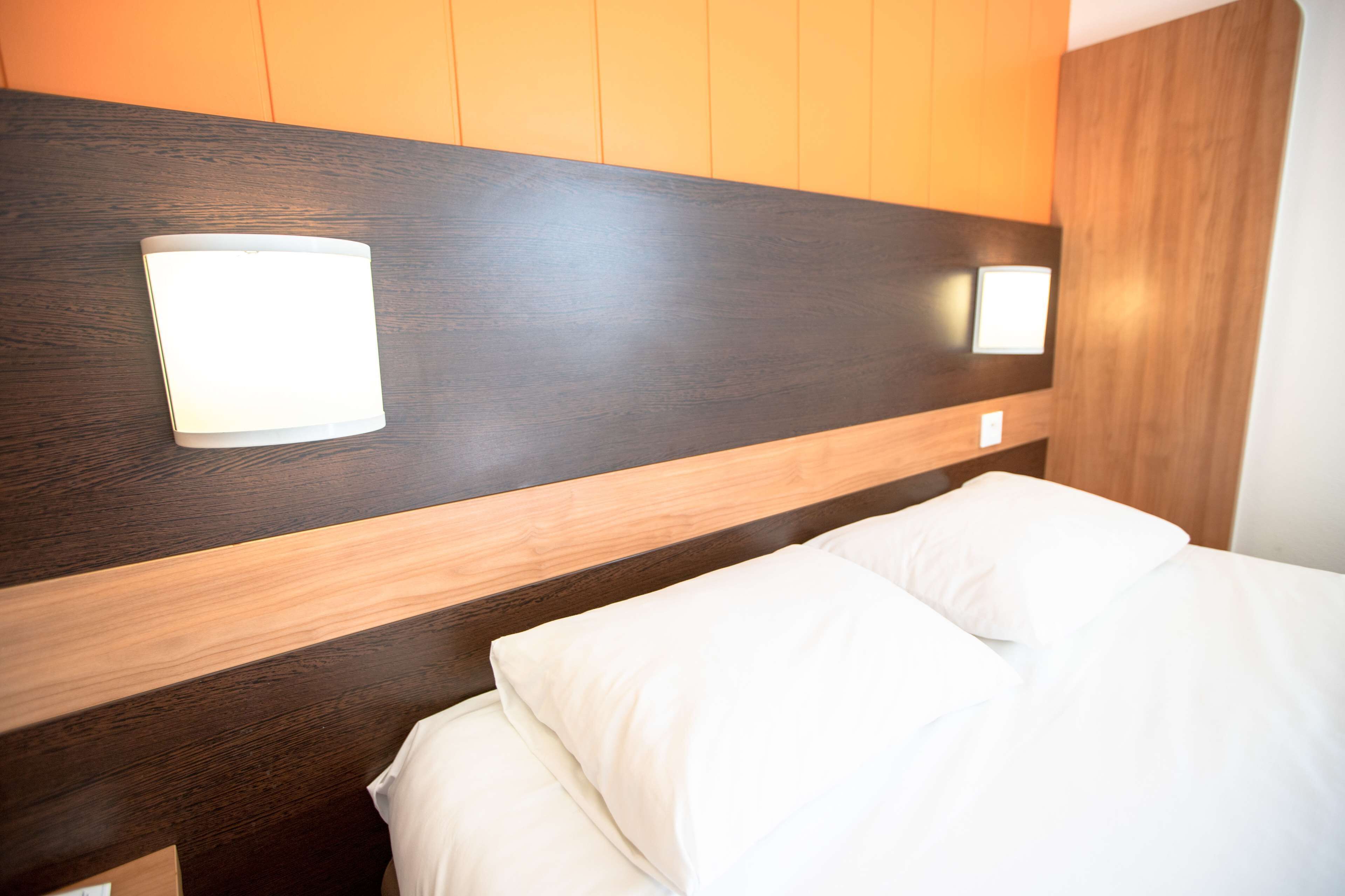 A modern hotel room with a wooden headboard, two bedside lamps, and white bedding.