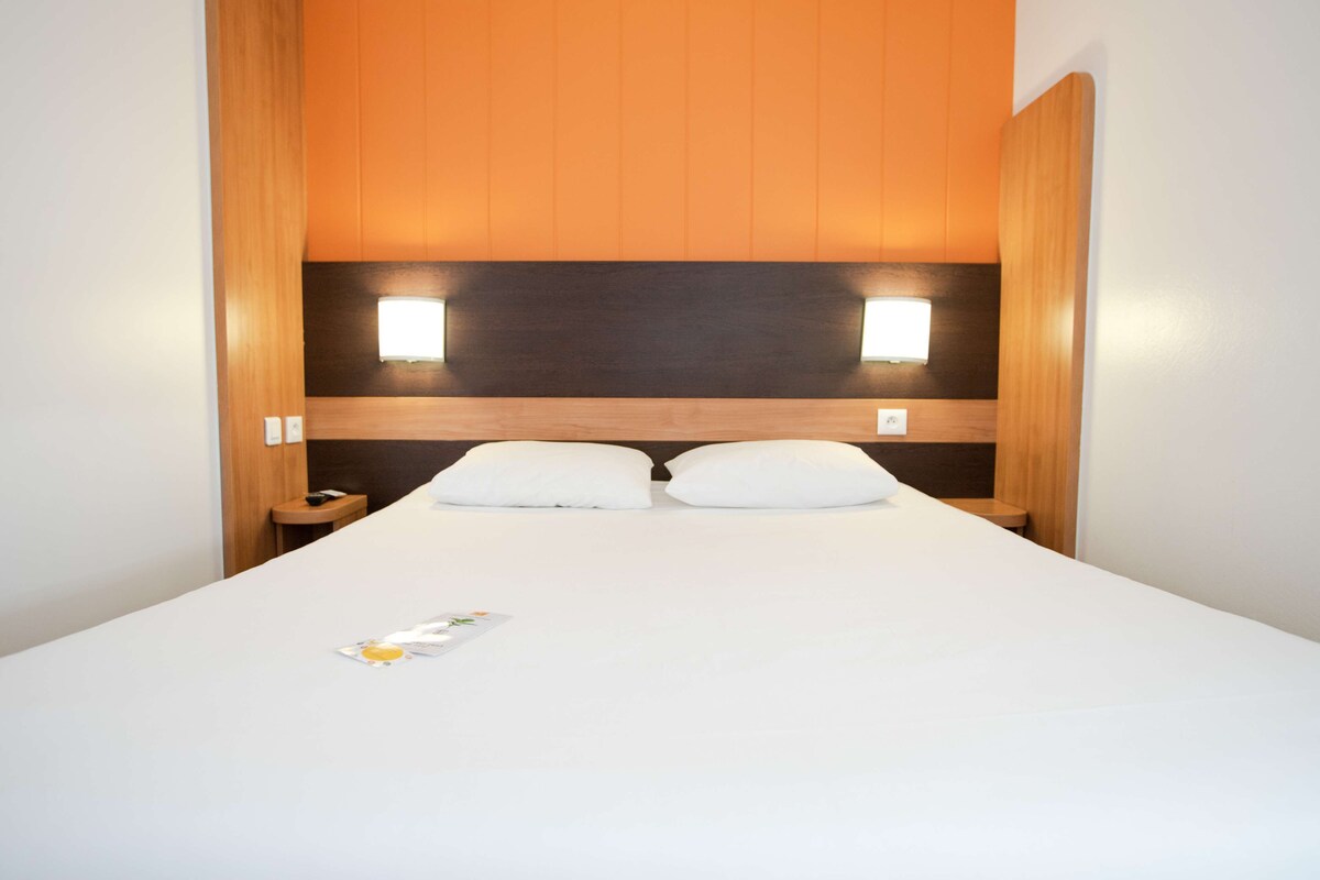 A hotel room with a large bed, two bedside tables, and a headboard with built-in lighting.