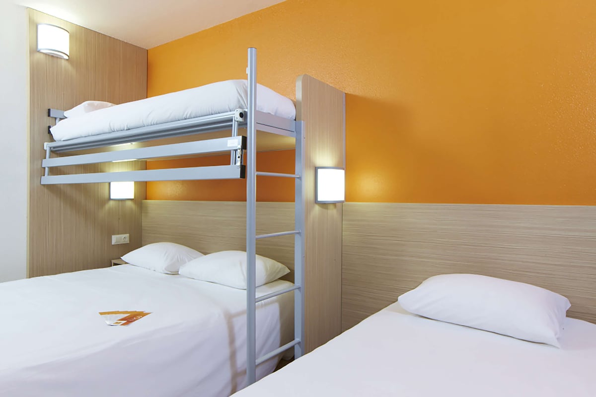A hotel room with two beds, one with a bunk bed and the other with a single bed.