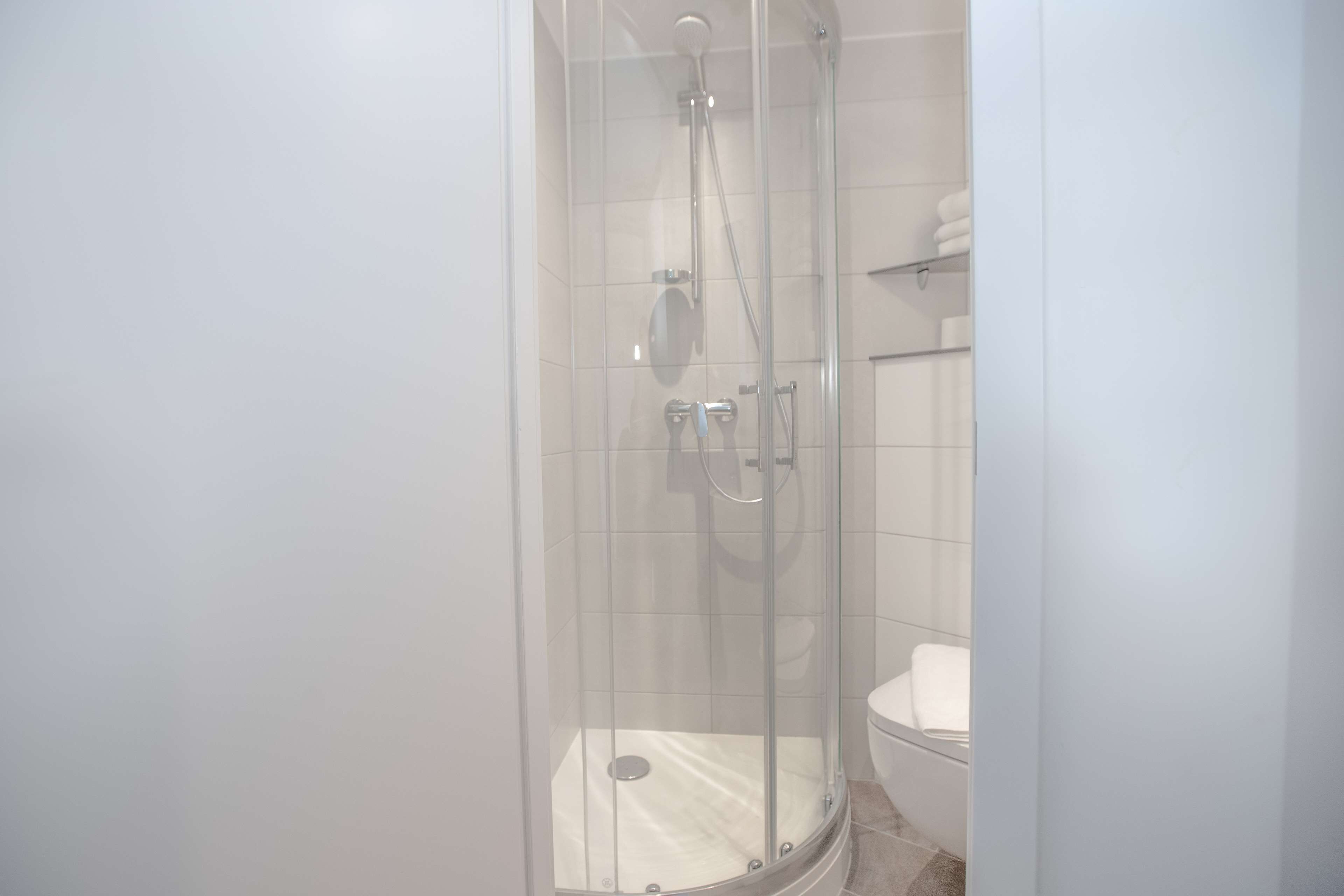 A glass-enclosed shower with a white toilet and a towel rack.