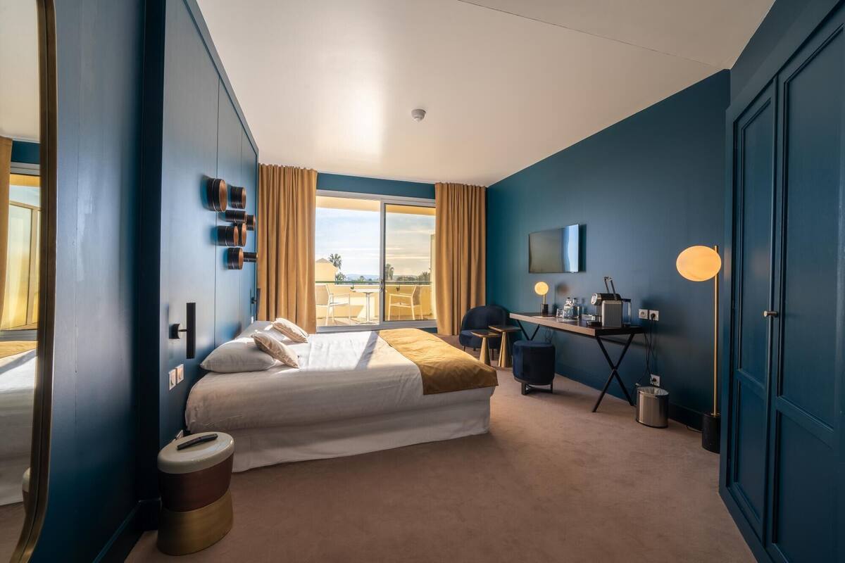A hotel room with a bed, a desk, a chair, a TV, and a window with curtains.