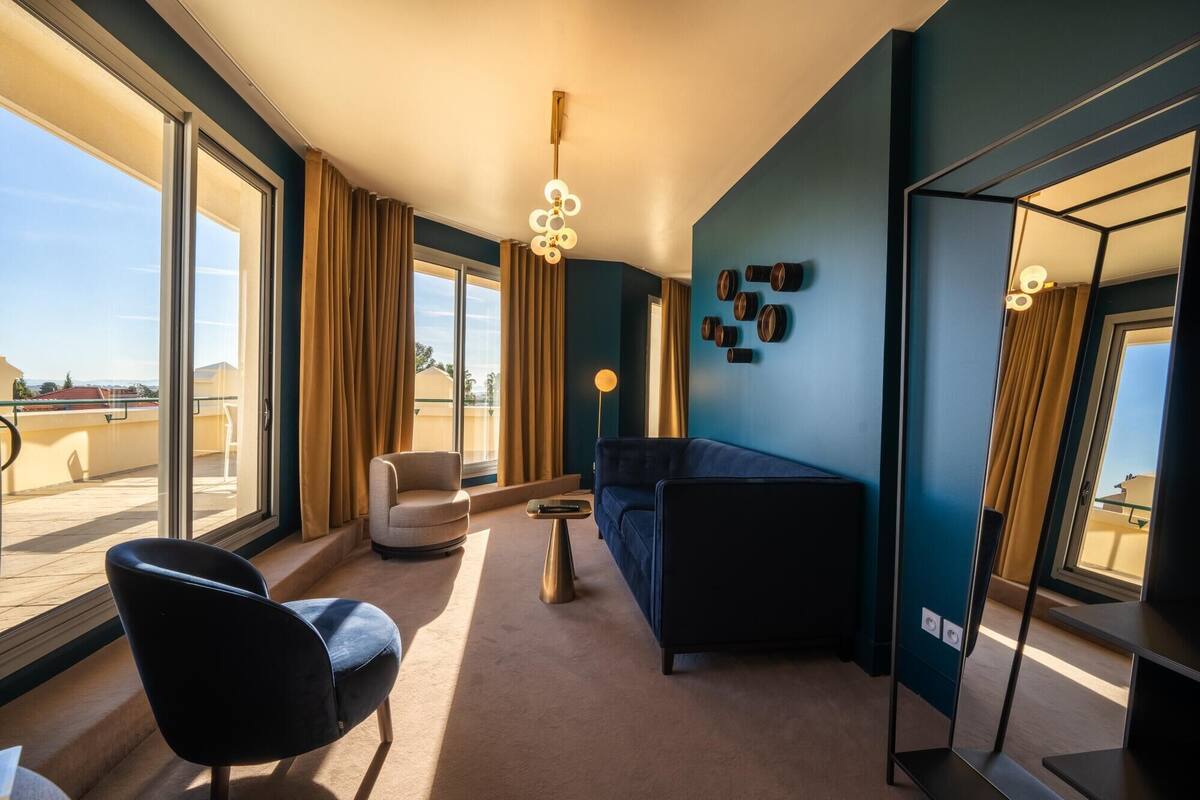 A modern hotel room with a large window, a sofa, a chair, and a small table.
