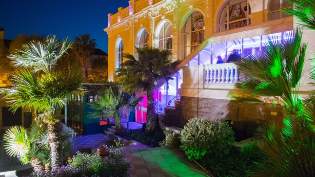 A historic building with arched windows and a courtyard with palm trees. - Hotel des Palmiers (Hyères)