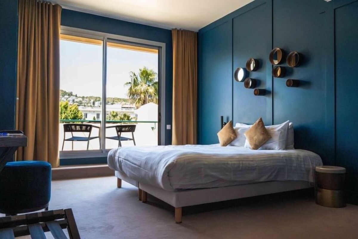 A bedroom with a bed, a desk, and a view of the outdoors.
