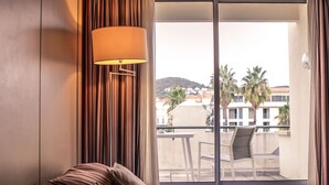 A hotel room with a bed, a lamp, and a view of the city through large windows. - Hotel des Palmiers (Hyères)
