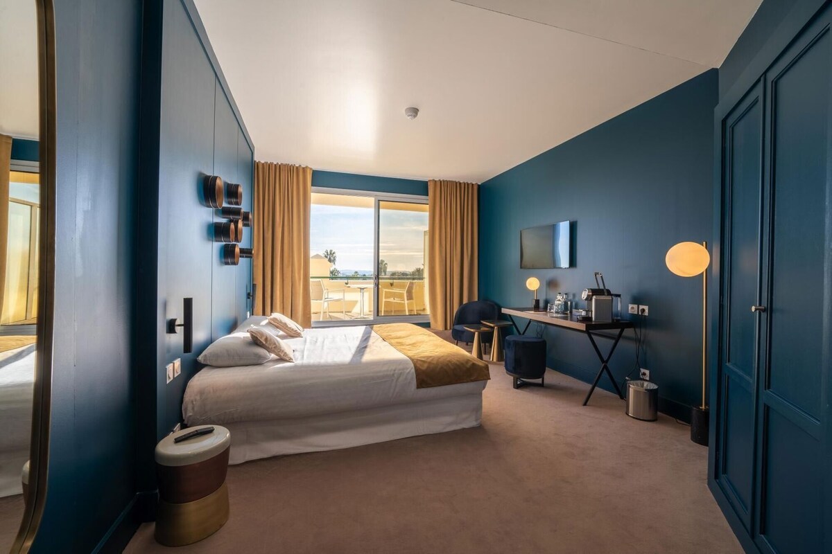 Habitación de hotel con cama, escritorio, silla y vistas al exterior.