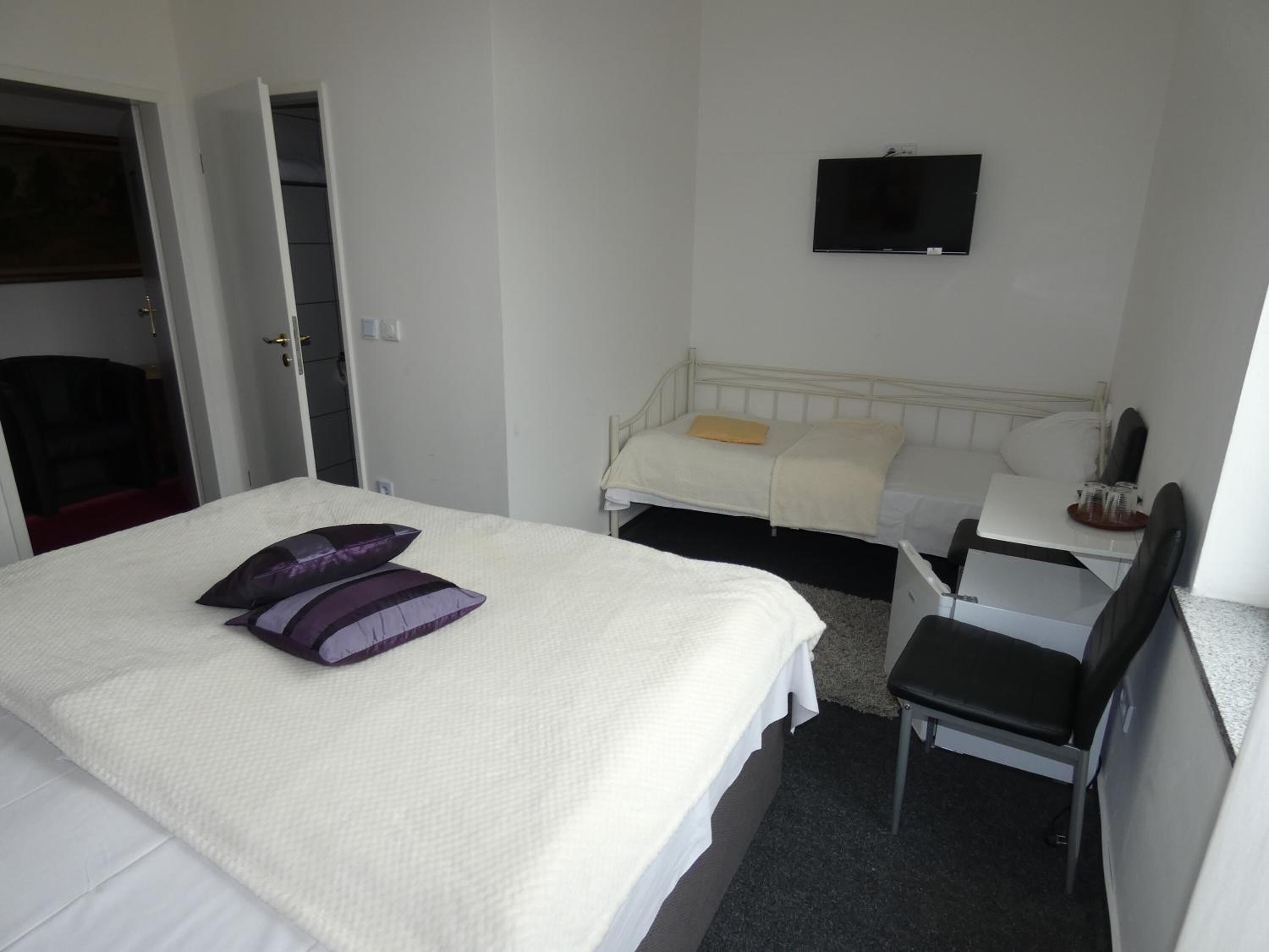 Quarto de hotel com cama, escrivaninha, cadeira, televisão e guarda-roupa.