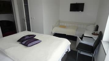 Quarto de hotel com cama, escrivaninha, cadeira, televisão e guarda-roupa.