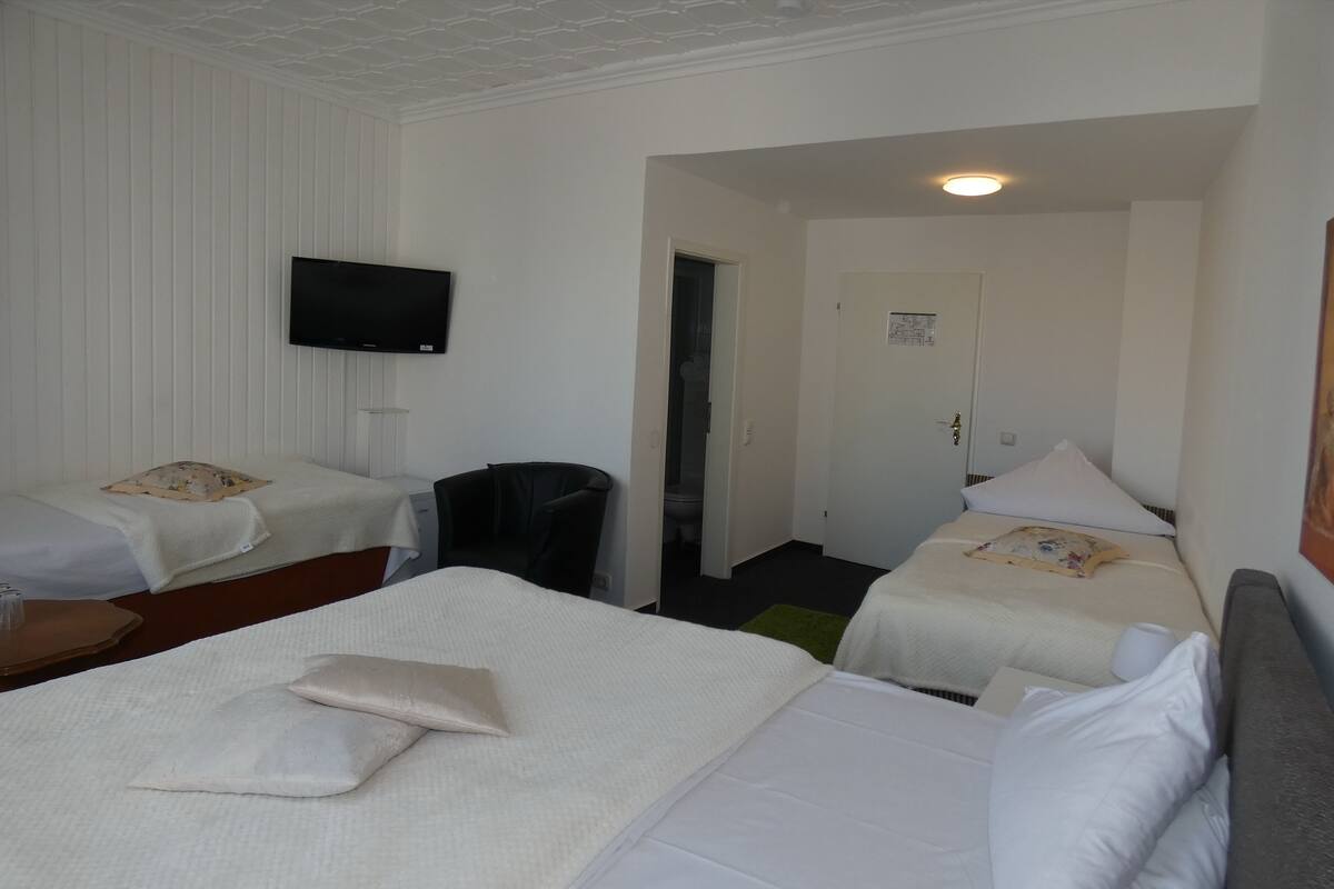 A hotel room with two beds, a TV mounted on the wall, a chair, and a small table.