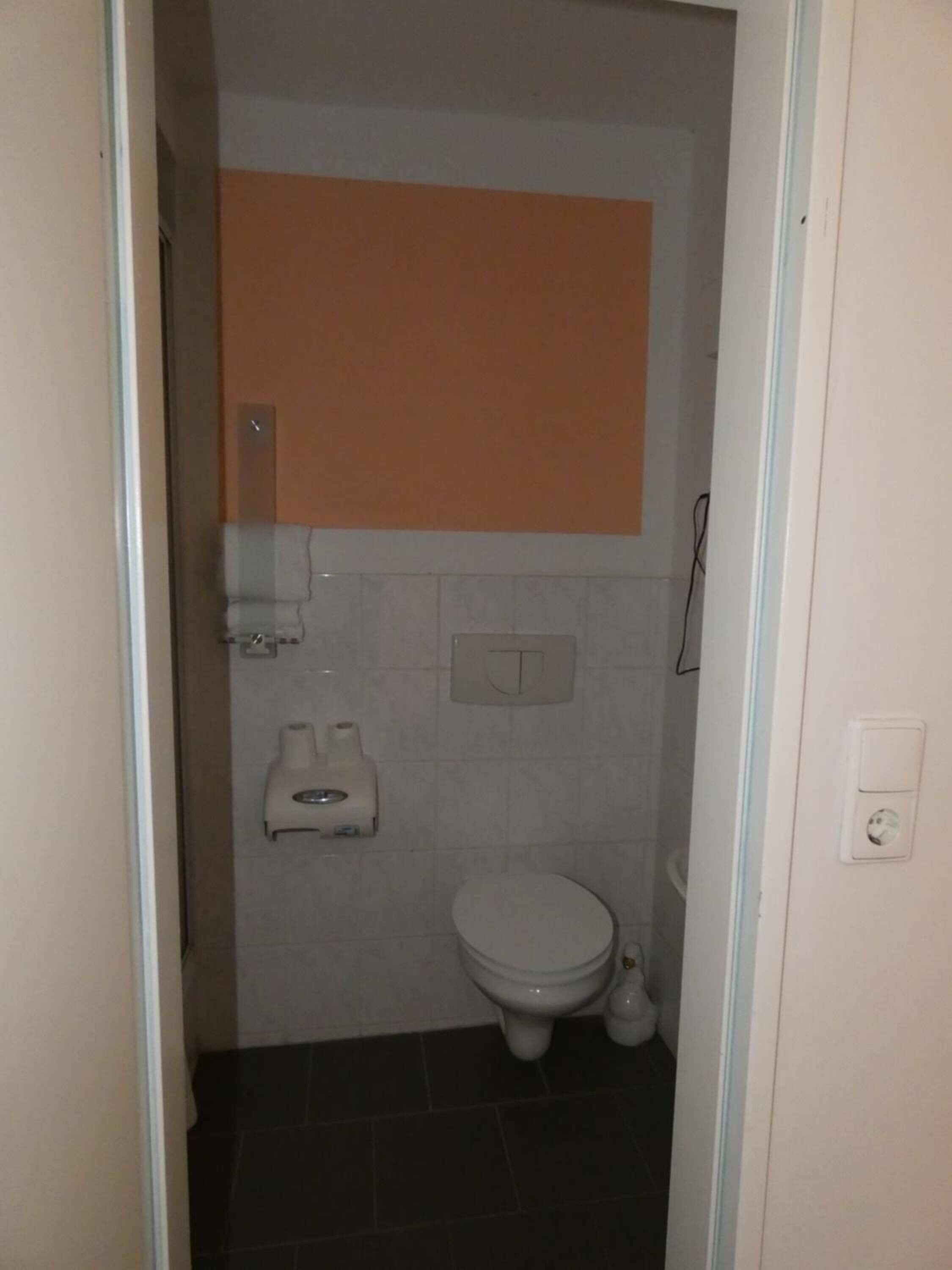 A small, narrow bathroom with a toilet, a sink, and a towel dispenser.